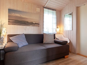Ett modernt vardagsrum med en grå soffa, ett litet bord med en vas med blommor och en tavla som föreställer ett landskap.