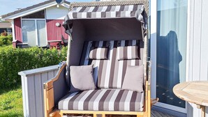 En randig loungestol för utomhusbruk med ett solskydd, placerad på ett trädäck med en glasdörr som leder ut till en trädgård.
