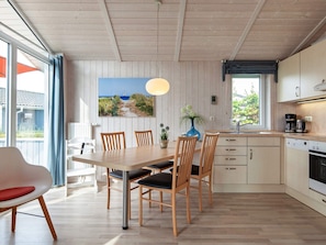 Ett modernt kök med träskåp, en matplats med bord och stolar samt ett stort fönster som ger utsikt över omgivningen.
