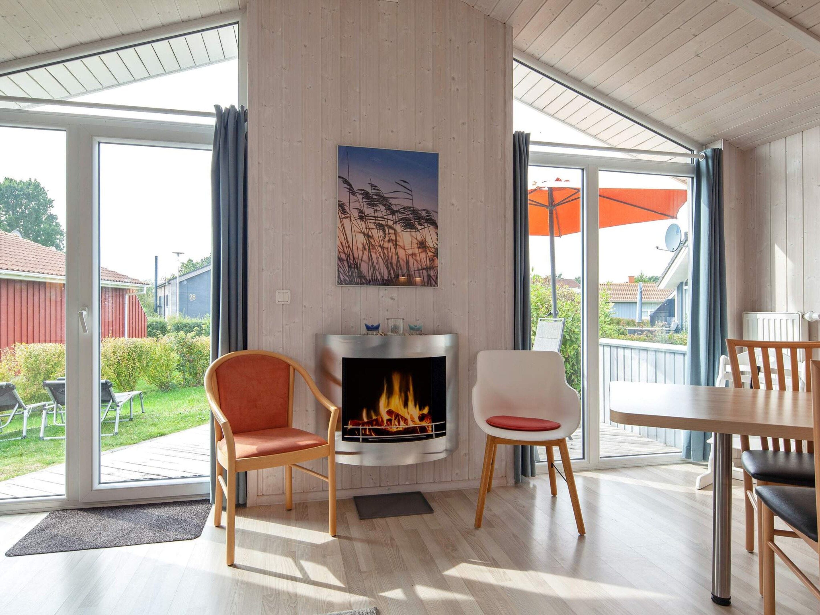 Ein modernes Wohnzimmer mit Kamin, zwei Sesseln, einem Tisch und einem großen Fenster mit Vorhängen.