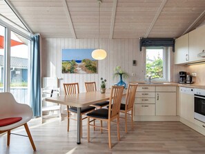 A modern kitchen with wooden cabinets, a dining table with chairs, and a large window with a view of the outdoors. - Holiday Home in GrÃ¶mmitz (Groemitz)