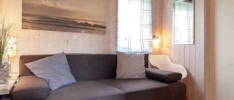 Un interior moderno con un sofá gris, una silla blanca y un cuadro de un paisaje.
