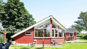 A red single-story house with large windows, a deck, and a garden.