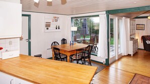 A kitchen with a wooden table and chairs, a white cabinet with silver handles, and a view of the outdoors through a glass door.