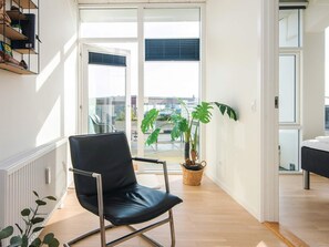 Un salon moderne avec un fauteuil en cuir noir, une plante en pot et une vue sur la ville grâce à de grandes fenêtres.