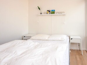 A minimalist bedroom with a bed, two bedside tables, a shelf with books and a plant, and a wall-mounted lamp. - 5 Star Holiday Home in Ringkobing (Ringkobing)