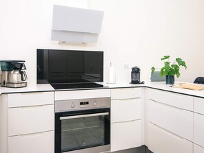 A modern kitchen with white cabinetry, a built-in oven, a coffee maker, and a potted plant. - 5 Star Holiday Home in Ringkobing (Ringkobing)