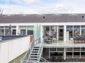 En modern byggnad med ett platt tak, stora fönster och en täckt uteservering med stolar och bord.