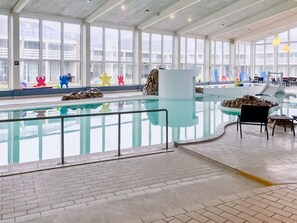 An indoor swimming pool with clear glass walls, a tiled floor, and a seating area with chairs and tables. - 5 Star Holiday Home in Ringkobing (Ringkobing)