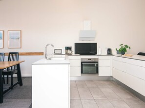 A modern kitchen with white cabinetry, a built-in oven, a microwave, and a coffee maker. There is a dining table with chairs and a small potted plant on the counter. - 5 Star Holiday Home in Ringkobing (Ringkobing)