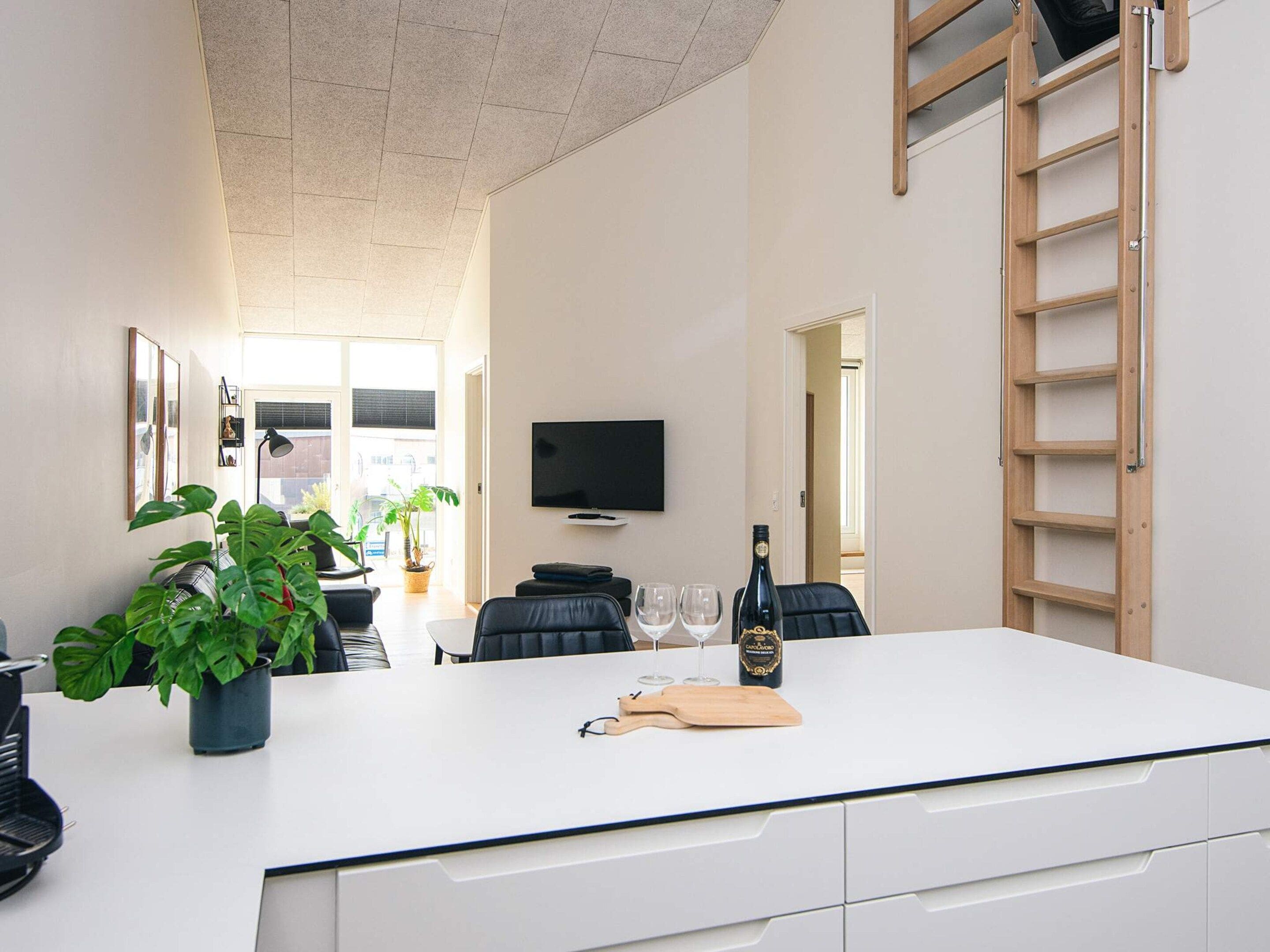 Cocina moderna con una isla central, un televisor montado en la pared y una escalera de madera.