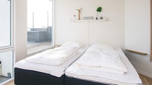 A minimalist bedroom with a bed, a window, and a shelf with a plant and a sign. - 5 Star Holiday Home in Ringkobing (Ringkobing)