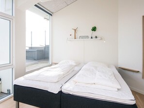 A minimalist bedroom with a bed, a window, and a shelf with a plant and a sign. - 5 Star Holiday Home in Ringkobing (Ringkobing)