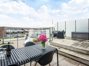 A rooftop terrace with a table, chairs, a flower vase, and outdoor furniture.