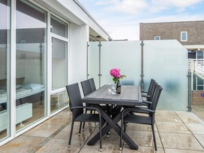Une terrasse avec une table et des chaises, un vase de fleurs et une cloison en verre.