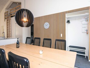 Un espace repas moderne avec une table en bois, des chaises noires, un luminaire suspendu, une horloge et un banc intégré.