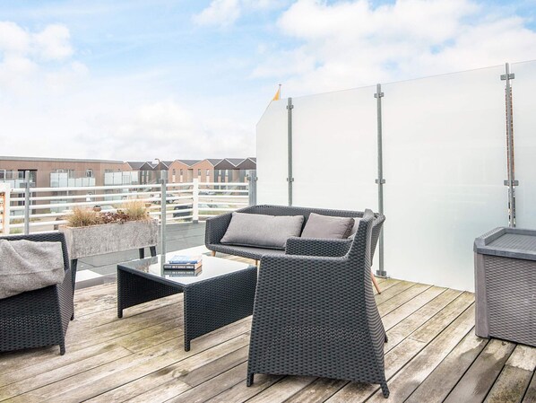 Une terrasse sur le toit, aménagée avec des meubles en osier et offrant une vue sur les immeubles d’habitation.
