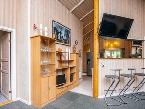 A wooden-paneled room with a TV mounted on the wall, a wooden cabinet with glassware, and a bar area with stools. - 4 Star Holiday Home in Ansager (Ansager)