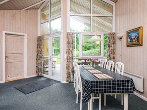 A dining area with a table set for four, large windows, and a view of greenery outside.