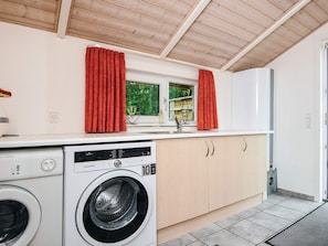 A compact kitchen with a washing machine, wooden cabinets, and a window with curtains.
