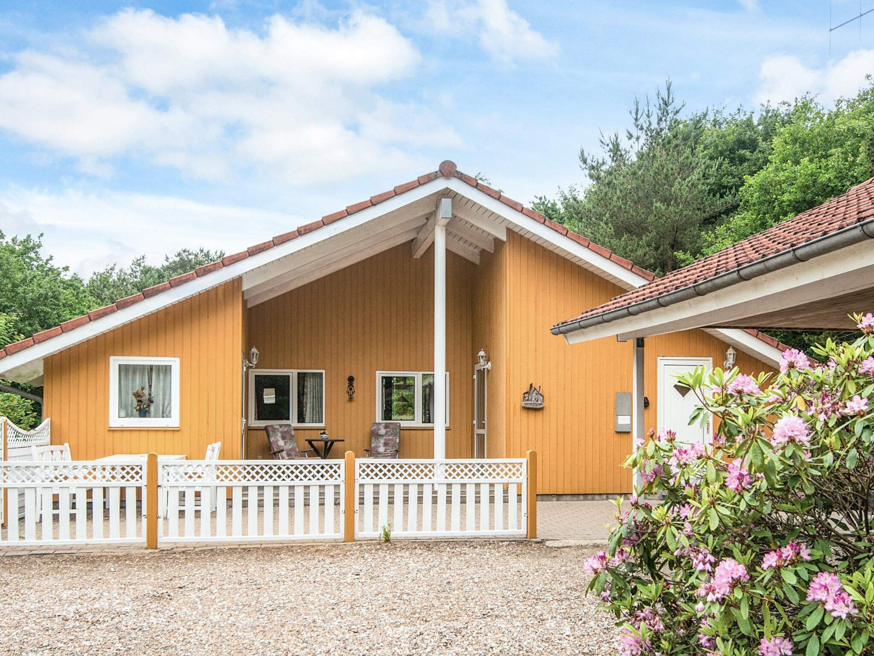 A wooden cabin with a porch, white picket fence, and a gravel driveway.