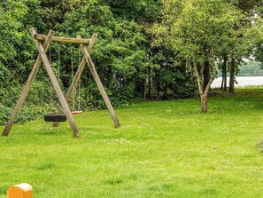 A wooden swing set in a grassy area with trees and a body of water in the background. - 4 Star Holiday Home in Ansager (Ansager)