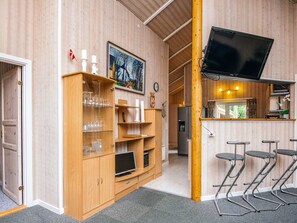 A wooden-paneled room with a television mounted on the wall, a wooden cabinet with glassware, and a bar area with stools.