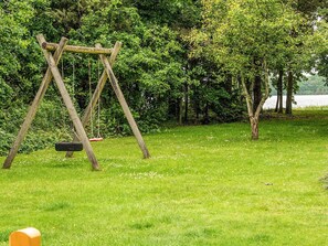 A wooden swing set in a grassy area with trees and a body of water in the background. - 4 Star Holiday Home in Ansager (Ansager)