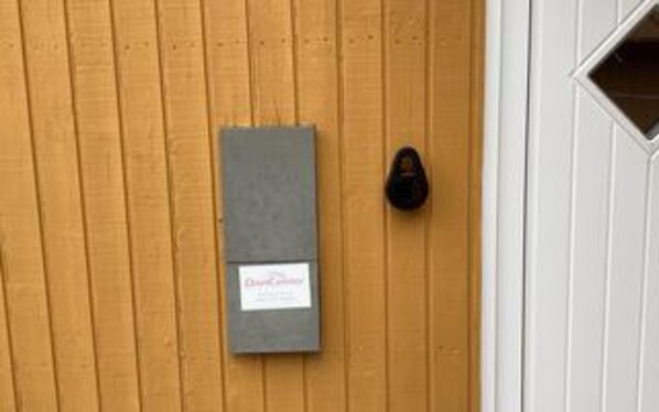 A wooden door with a gray intercom box and a black doorbell.