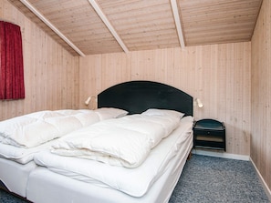 A bedroom with a wooden ceiling, a black headboard, a bed with white bedding, a nightstand, and a red curtain.