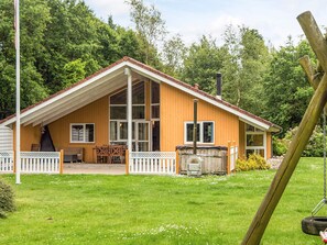 A wooden cabin with a large porch, a chimney, and a grill area. - 4 Star Holiday Home in Ansager (Ansager)