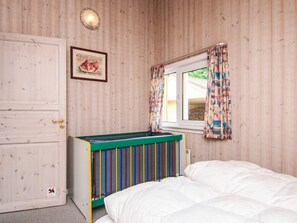 A bedroom with a wooden wall, a window with patterned curtains, a bed with white bedding, and a colorful bunk bed. - 4 Star Holiday Home in Ansager (Ansager)