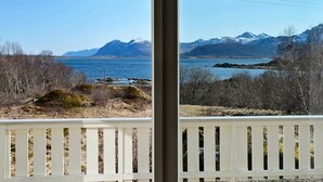 A view from a balcony with a white railing, overlooking a body of water, mountains, and sparse vegetation. - Holiday Home in Leknes (Vestvågøy)