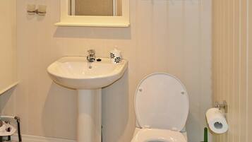 A bathroom with a pedestal sink, toilet, and a small shelf above the sink.