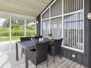 A covered patio with a table and chairs, large windows, and a view of greenery. - 4 Star Holiday Home in Hjorring (Hjørring)