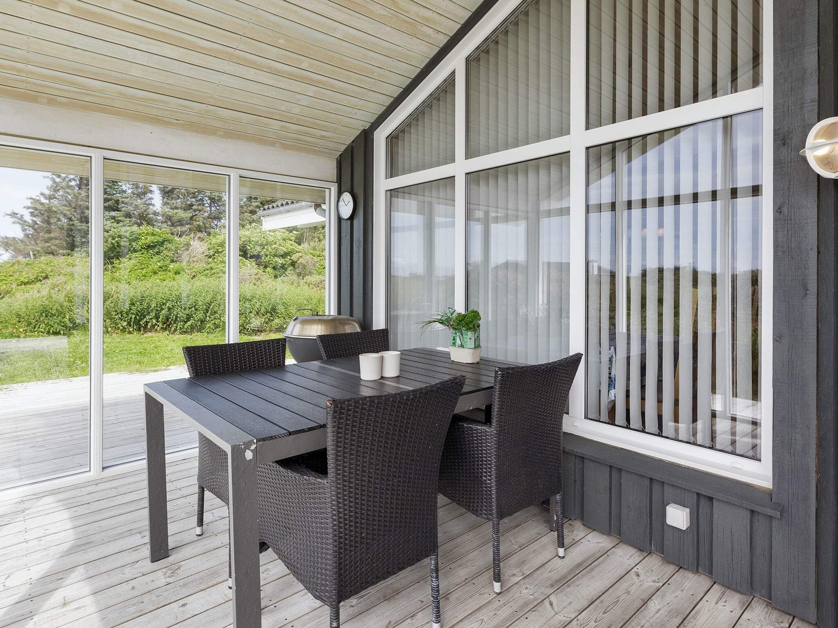 Un patio al aire libre con mesa y sillas, ventanas amplias y vista a follaje.