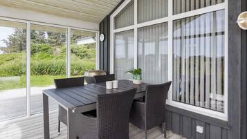 Un patio al aire libre con mesa y sillas, ventanas amplias y vista a follaje.