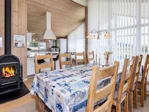 Un comedor acogedor con estufa de leña, sillas de madera y una mesa cubierta con mantel estampado.