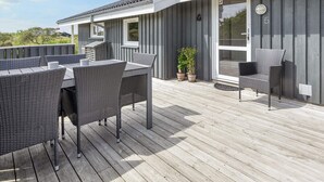 A covered outdoor deck with a table and chairs, a potted plant, and a sliding glass door.