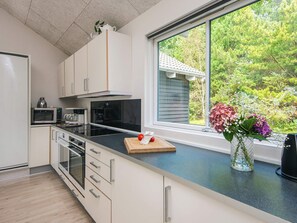 A modern kitchen with white cabinetry, a black countertop, and a large window offering a view of trees.