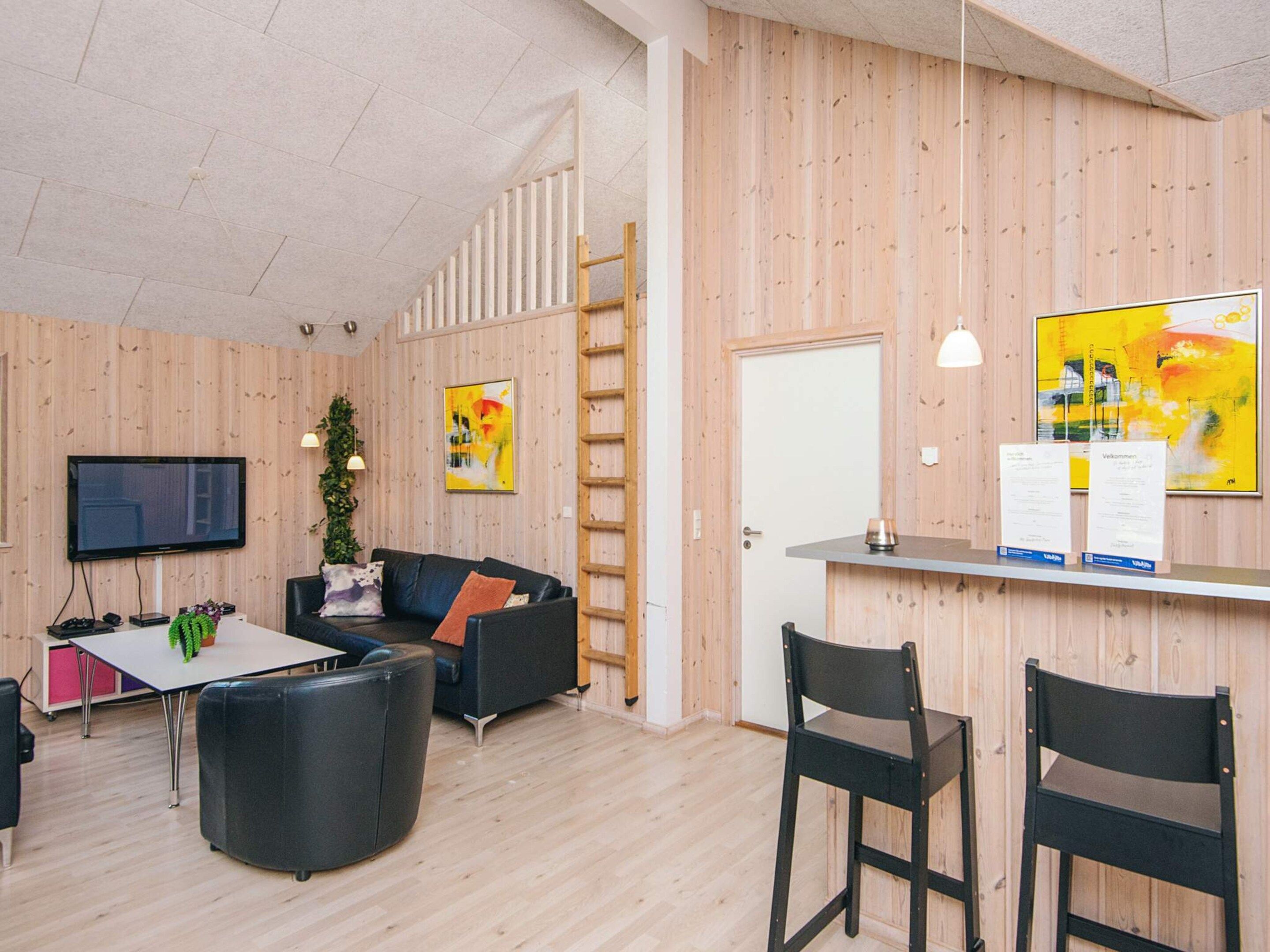 Un espace de bureau moderne avec un intérieur en bois, un grand téléviseur à écran plat, un canapé en cuir noir, une petite table et deux chaises noires.