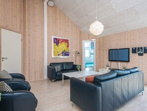 A modern living room with a wooden wall, a black leather sofa, a white coffee table, and a flat-screen TV mounted on the wall.