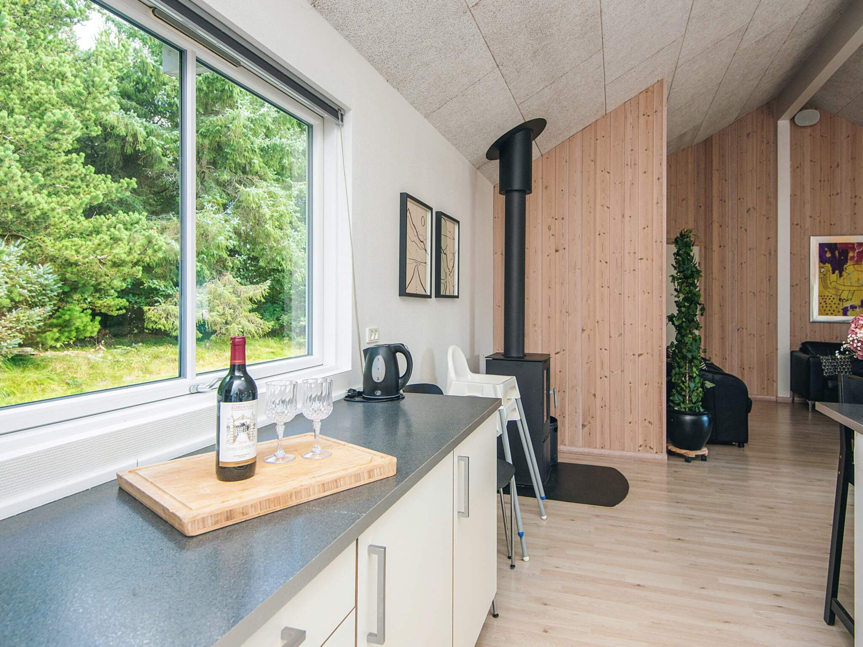 A modern kitchen with a large window, a wine bottle, and glasses on the counter.