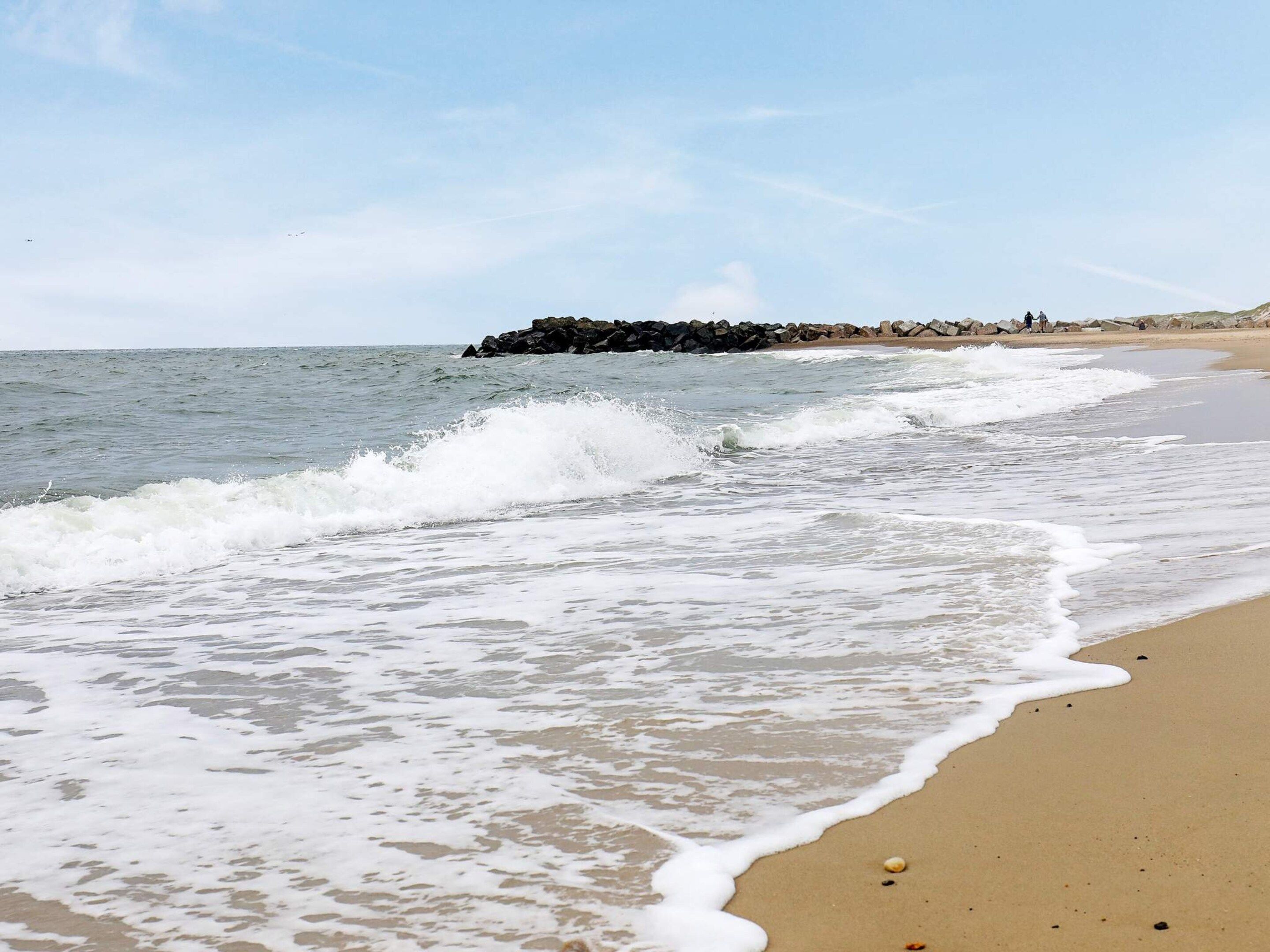 A beach with waves, a rocky outcrop, and a clear sky.
