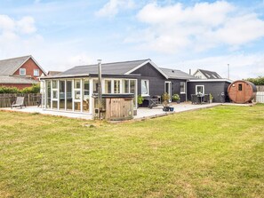 A modern house with a glass-enclosed patio, a wooden barrel, and a well-maintained lawn. - 4 Star Holiday Home in Ulfborg (Ulfborg)