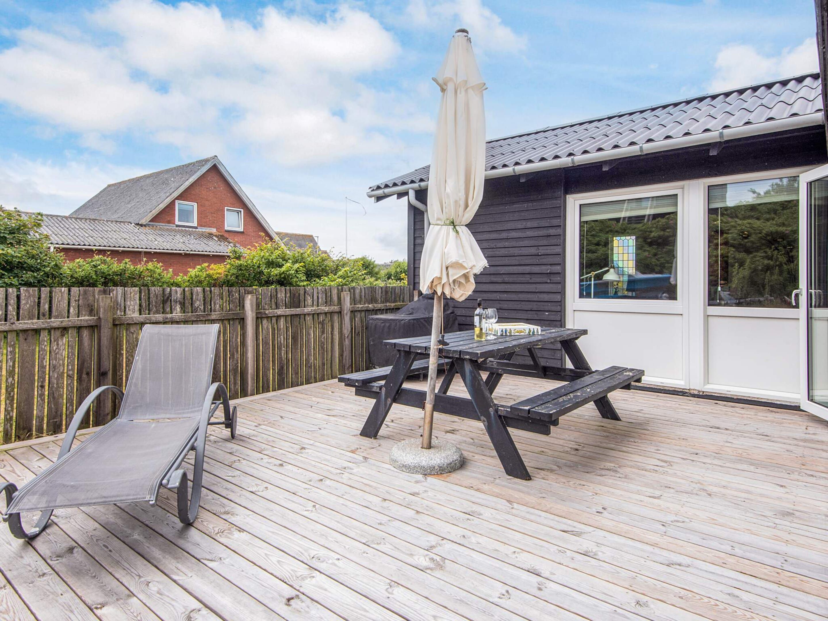 A wooden deck with a table and chairs, a grill, and a covered umbrella.
