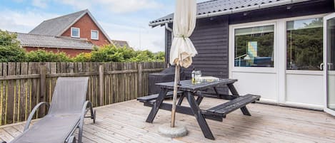 A wooden deck with a table and chairs, a grill, and a covered umbrella.