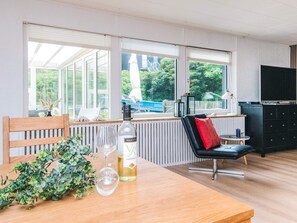A modern kitchen with large windows, a dining table with a bottle of wine, and a black chair with a red pillow. - Luxury Spa Retreat in Thorsminde (Ulfborg)