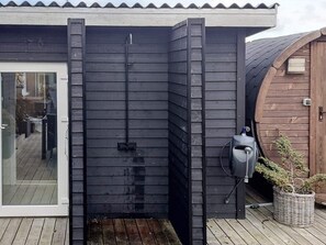 A modern outdoor shower area with a sliding door, a small step leading up to it, and a wooden deck surrounding the space. - 4 Star Holiday Home in Ulfborg (Ulfborg)