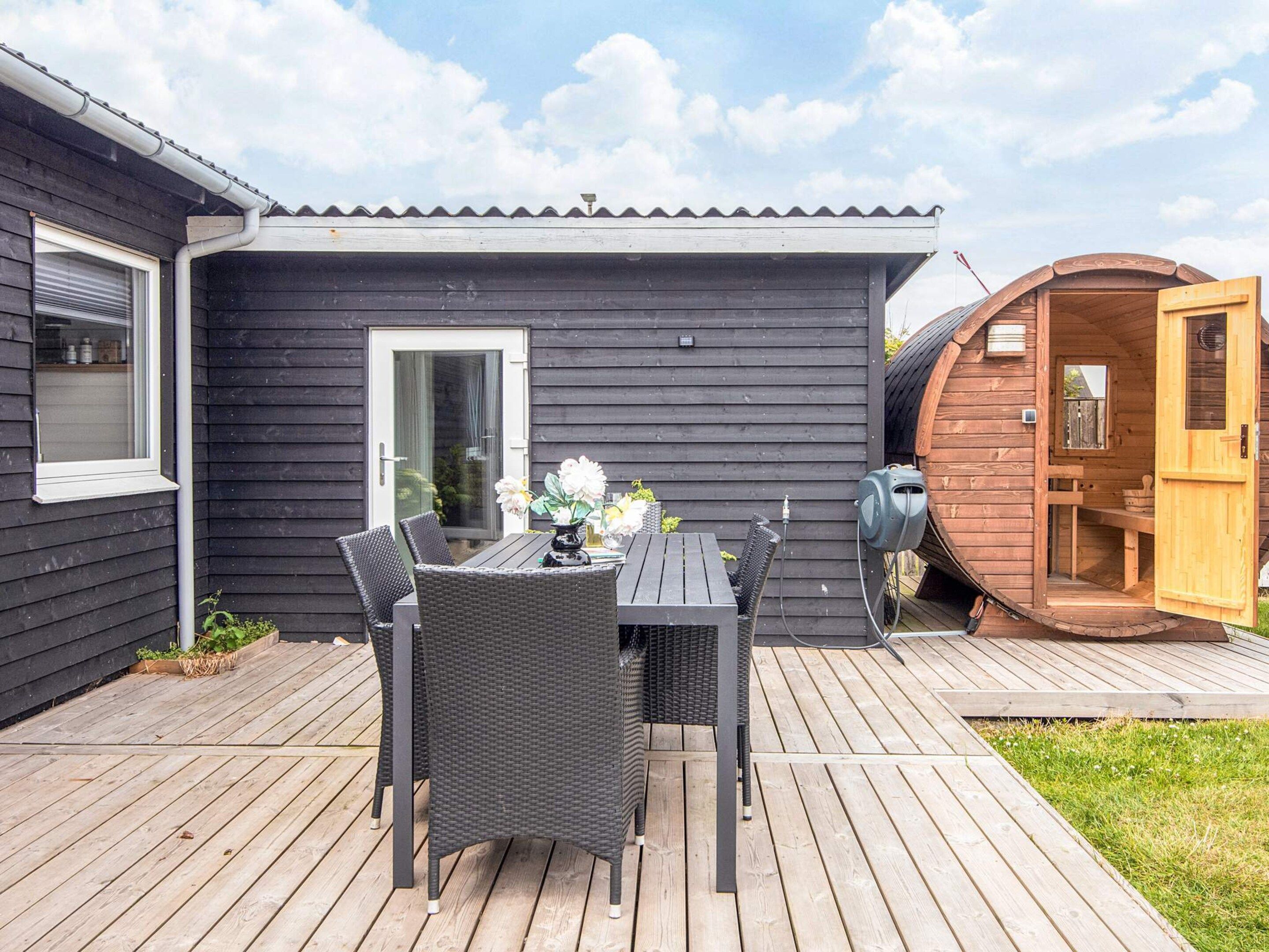 Una terraza de madera con una mesa y sillas, un jardín pequeño y una sauna.